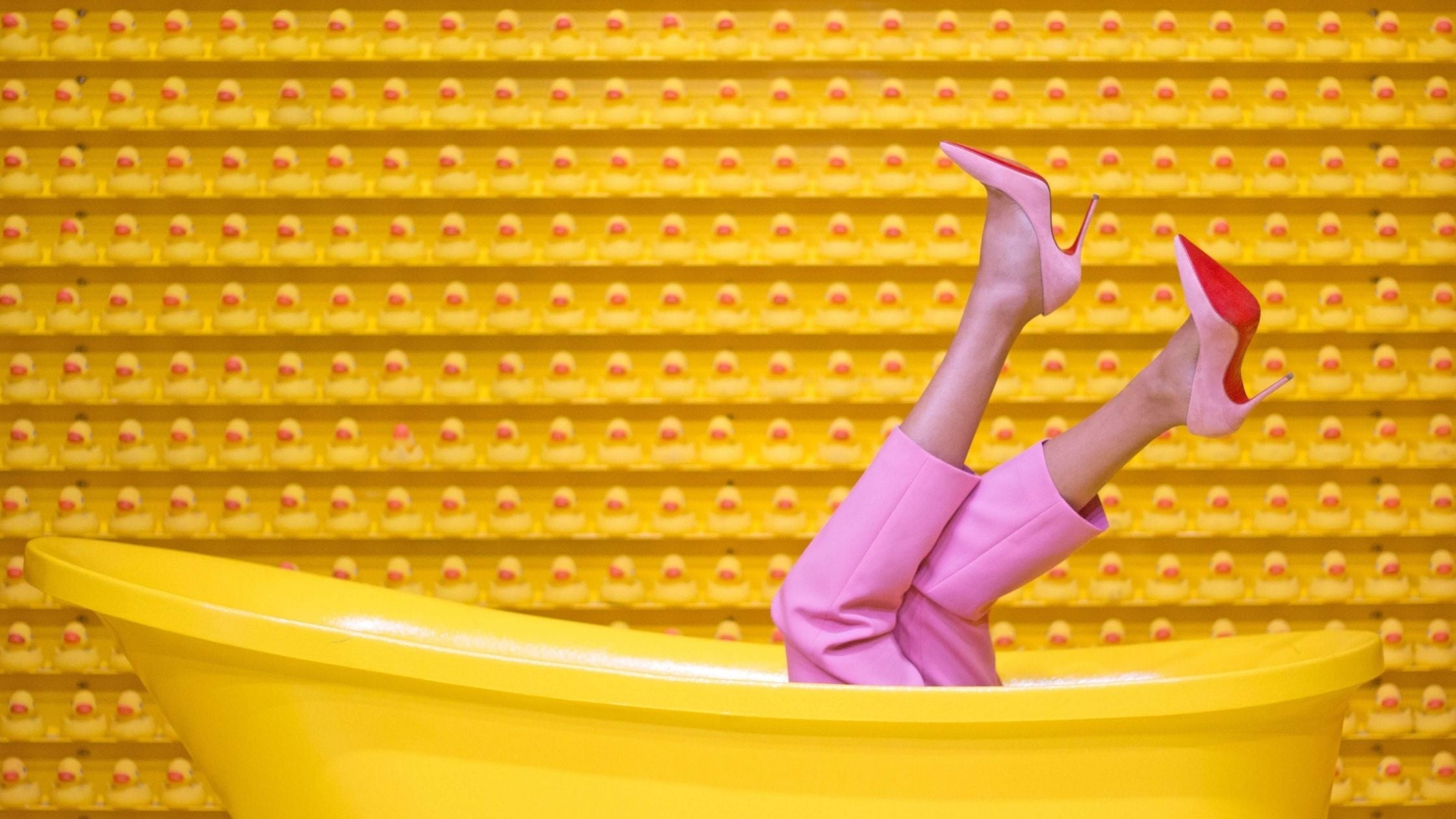 Lady in pink shoes and pants lying in a all yellow tub.