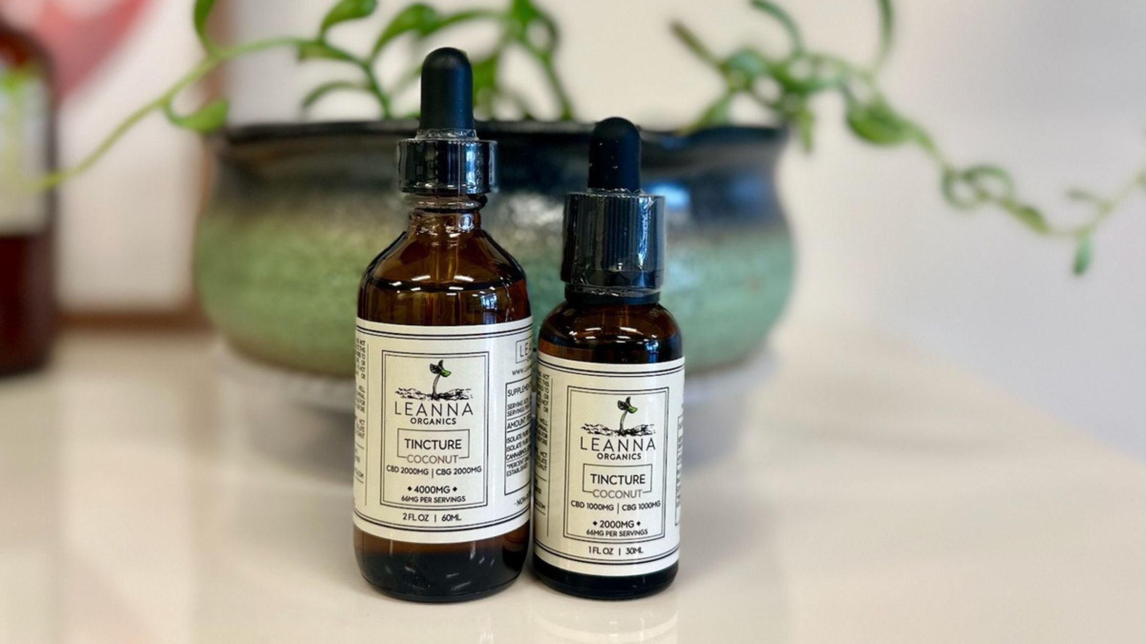 CBD oil by Leanna Orgnaics on a table with a plant behind it.