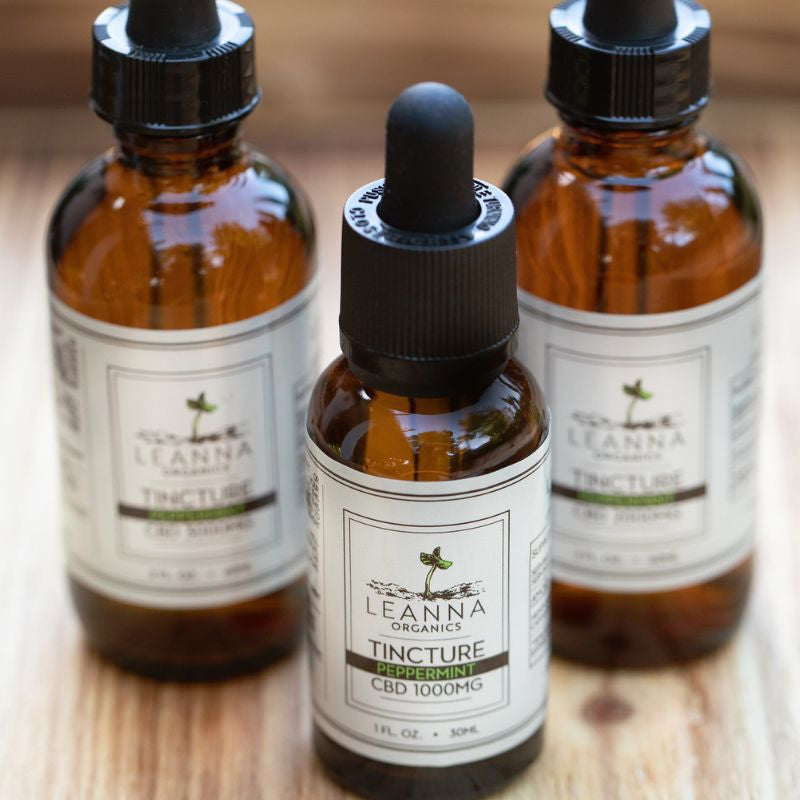 Three bottles of Leanna Organics CBD tinctures on a wooden surface