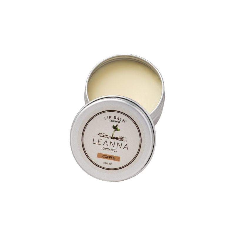 An open silver metal tin of Leanna Organics Coffee lip balm, showing the pale yellow balm inside, with the lid placed in front displaying the brand label.
