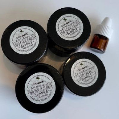 Four black containers with white labels containing Leanna Organics CBD sample products on a light background.