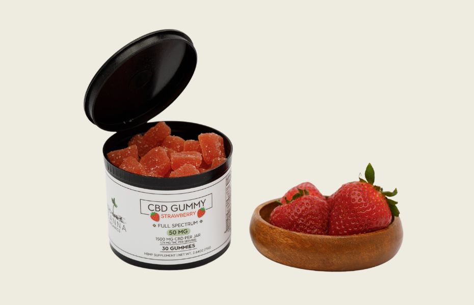 Open container of CBD gummies with a bowl of strawberries on a beige background