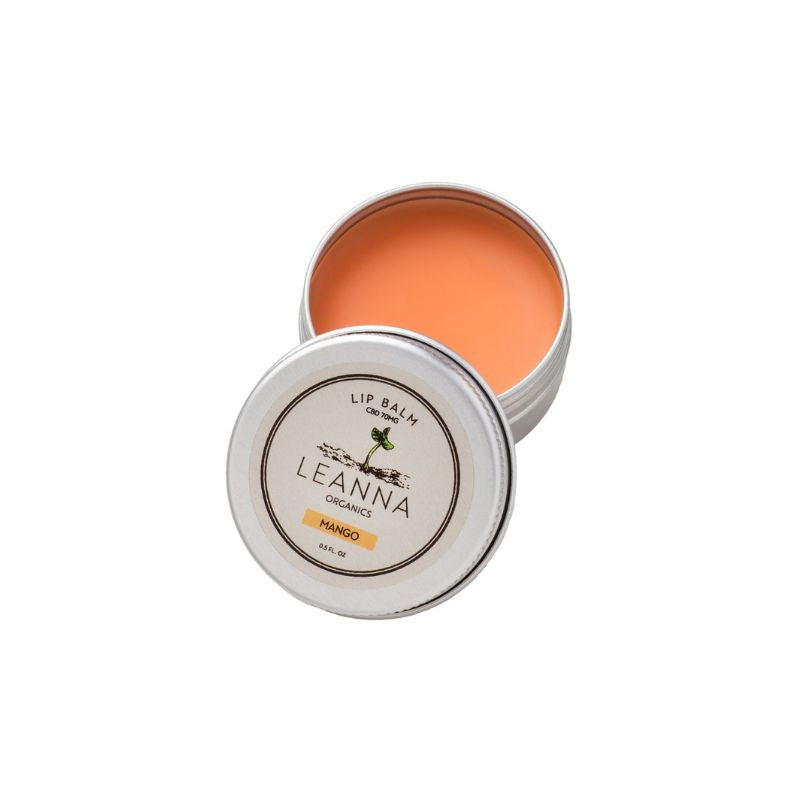 An open round metal tin of Leanna Organics Mango CBD lip balm, showing the bright orange balm inside, with the lid placed in front displaying the brand label.