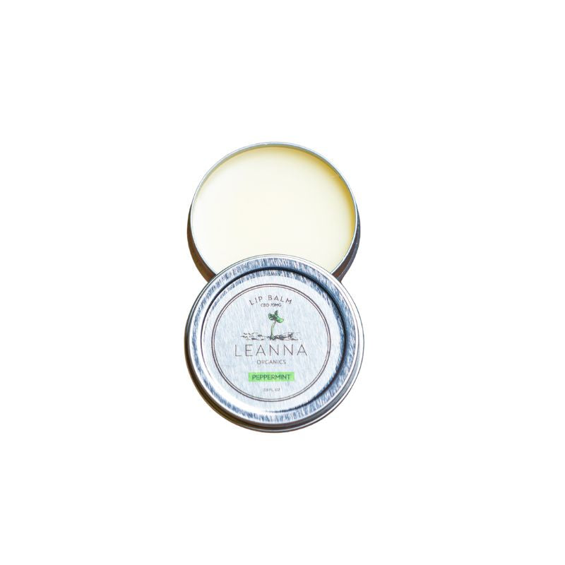 An open round metal tin of Leanna Organics CBD lip balm, showing the pale yellow balm inside and the silver lid.